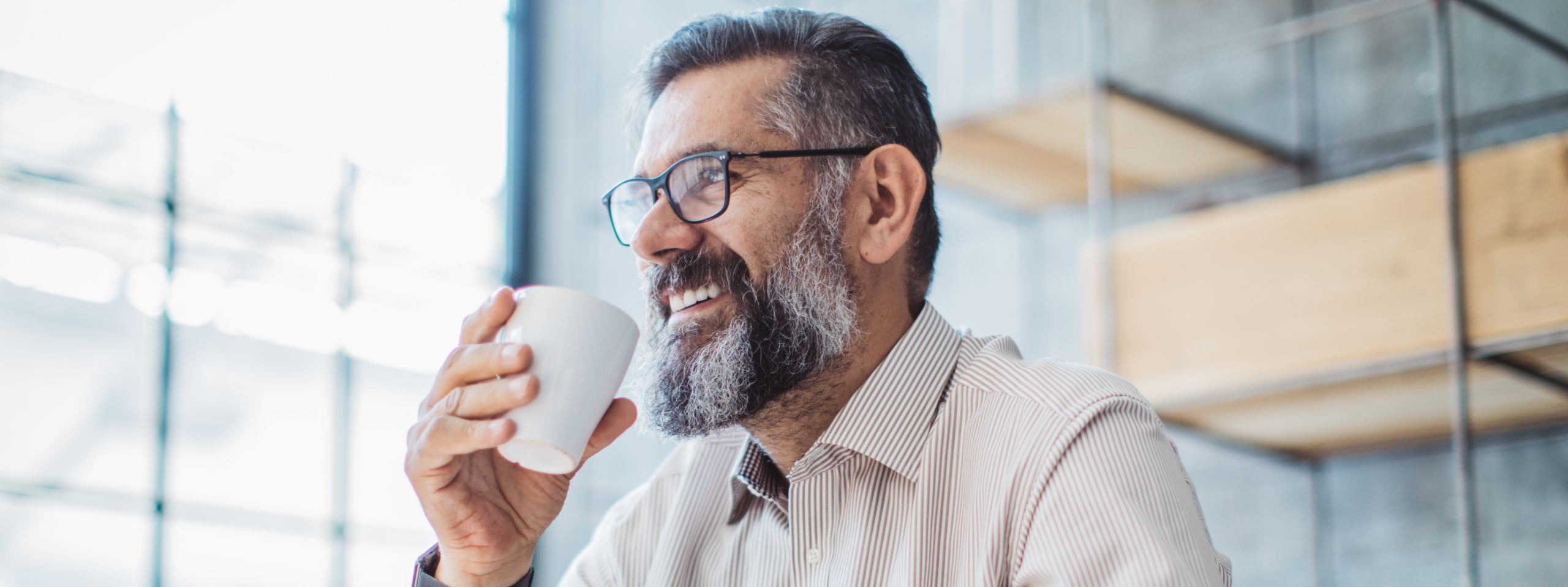 Mann mit grauem Bart und Brille trinkt Kaffee.